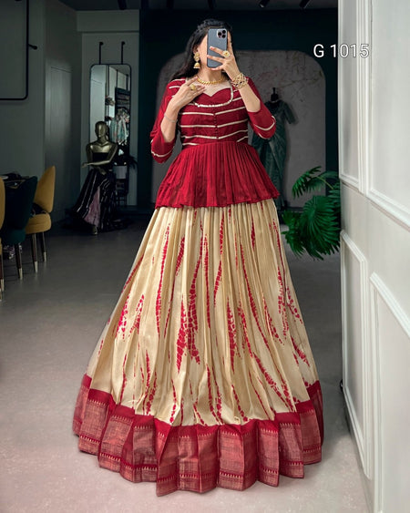 A woman takes a mirror selfie wearing a traditional Indian outfit consisting of a deep red sleeveless top with a peplum waist and a matching voluminous beige skirt with red tie-dye patterns and a red border. The background shows a boutique interior with mannequins and clothing racks.