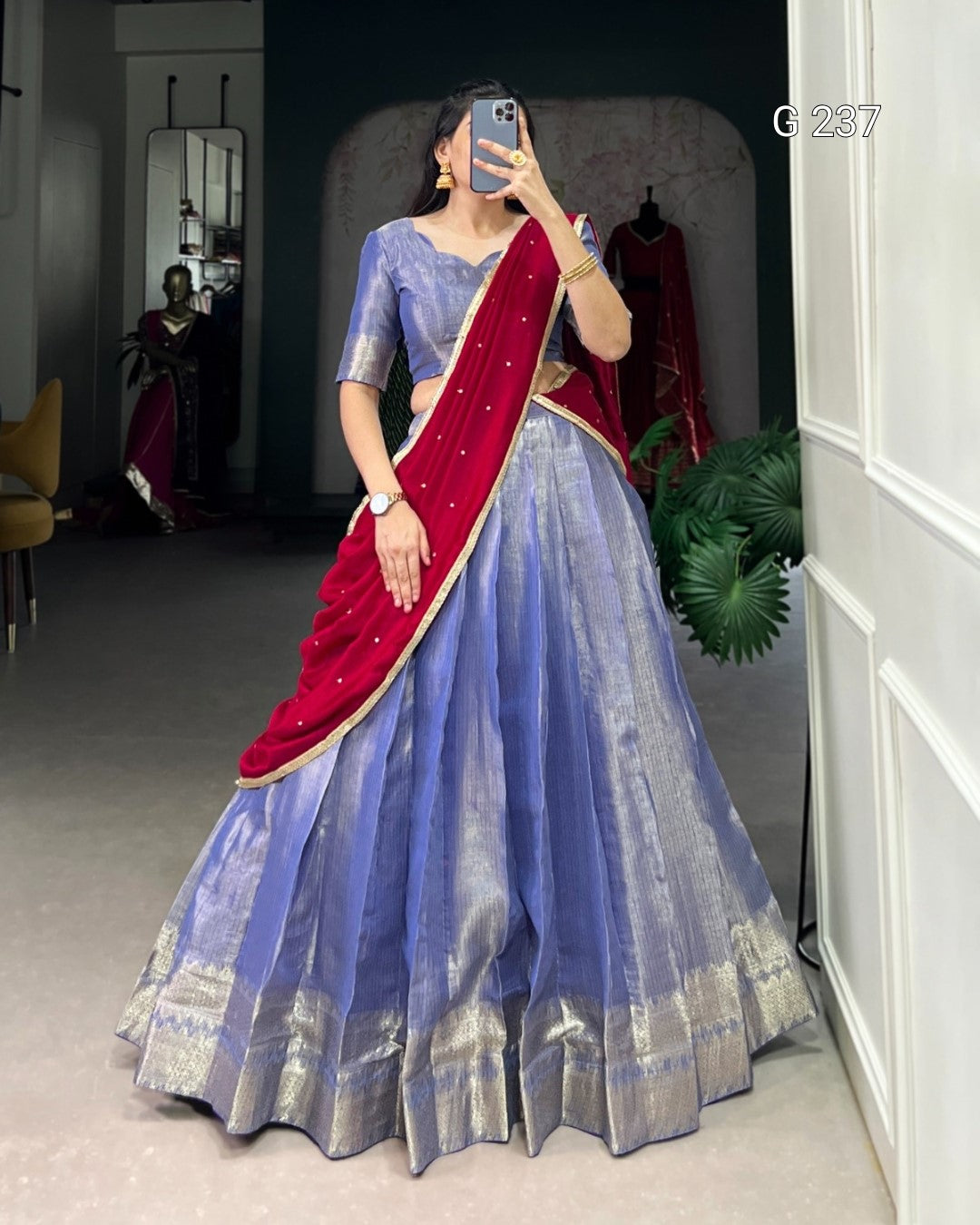 Woman in a blue saree with red blouse taking a mirror selfie in a room.