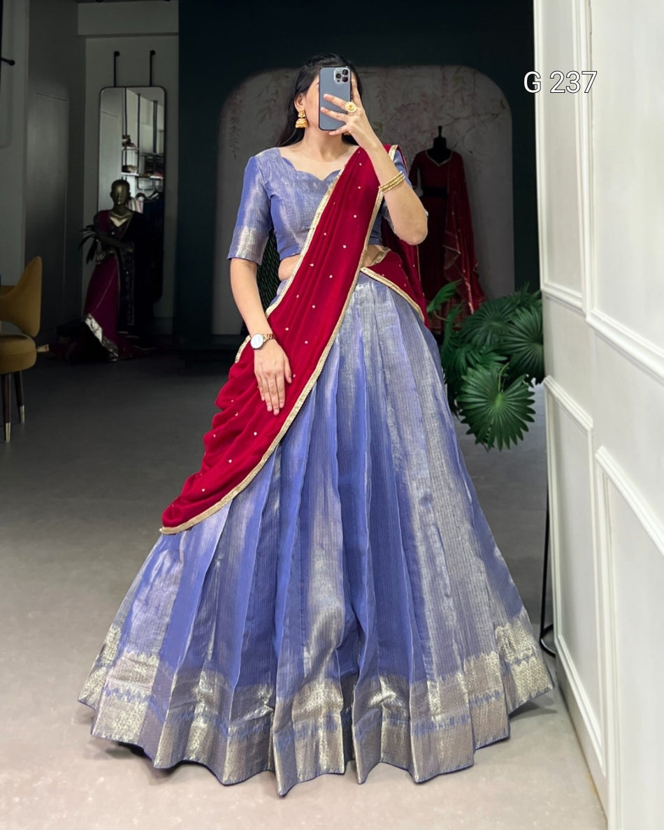 Woman in a blue saree with red blouse taking a mirror selfie in a room.