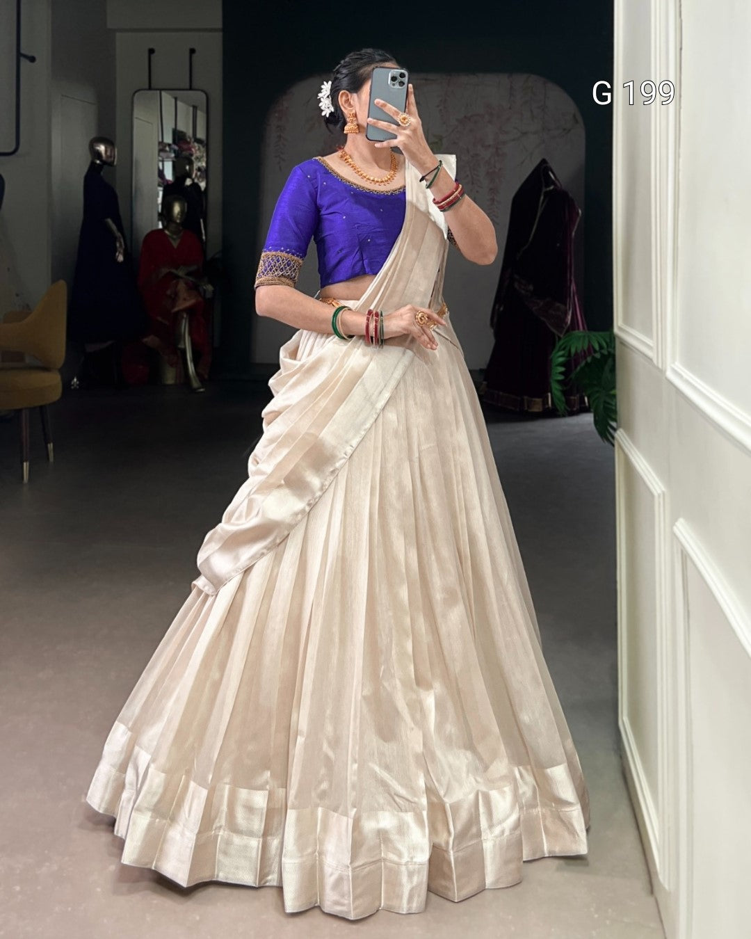 Person wearing a traditional outfit with a blue blouse and white saree in an indoor setting.