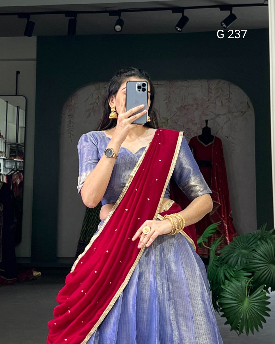 Woman taking a mirror selfie wearing a blue saree with a red border indoors.
