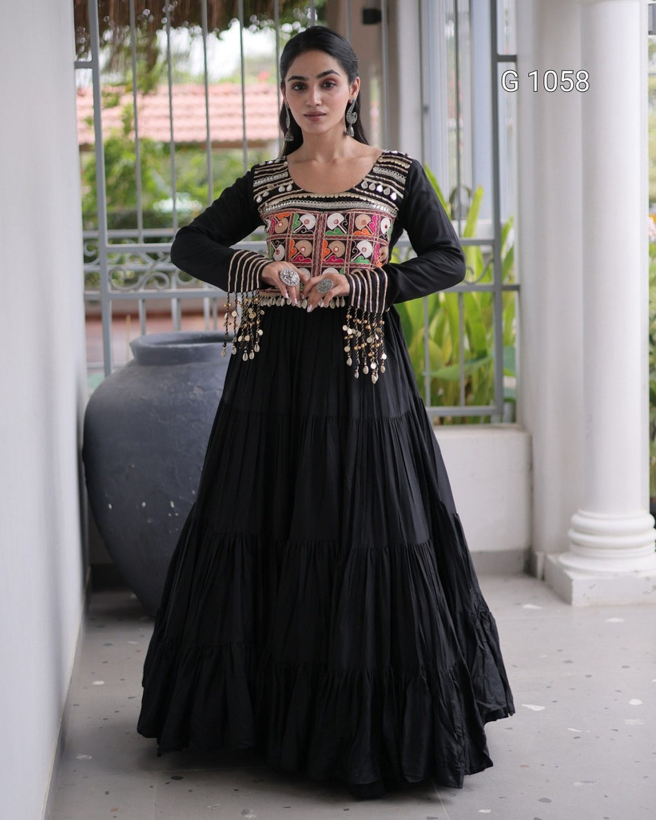 A woman models a black long-sleeve Anarkali gown with a heavily embroidered multicolor neckline and gold-toned embellishments on the sleeves, set against a white-pillared outdoor corridor.