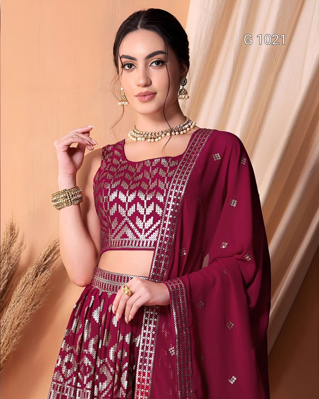 A woman models a deep maroon traditional Indian ethnic wear set consisting of a patterned crop top, matching flared skirt, and a sheer dupatta with silver mirror work borders, set against a warm beige backdrop.