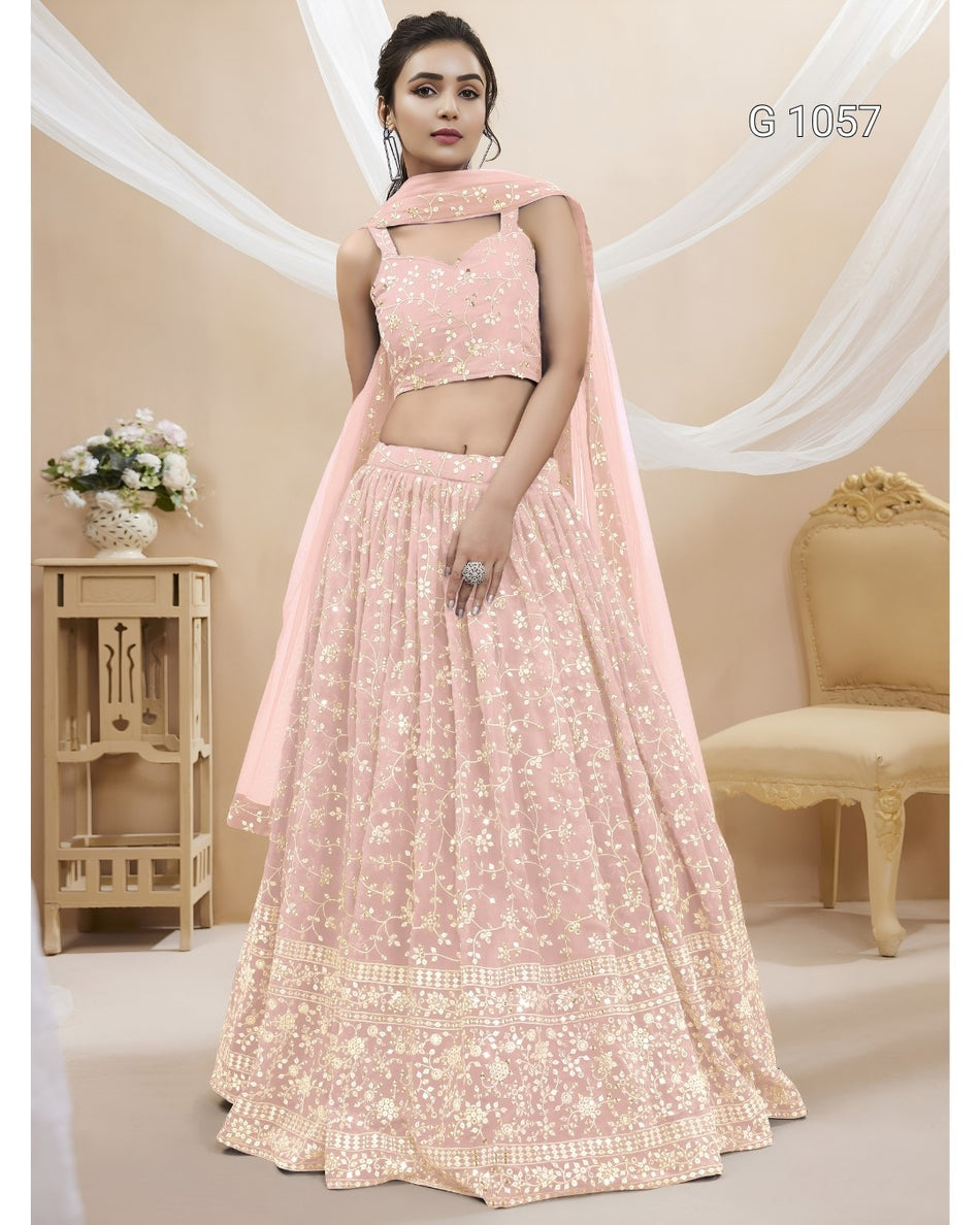 A woman models a light pink embroidered Indian ethnic wear set consisting of a sleeveless crop top, a long flared skirt, and a matching dupatta. The set features intricate white floral embroidery.