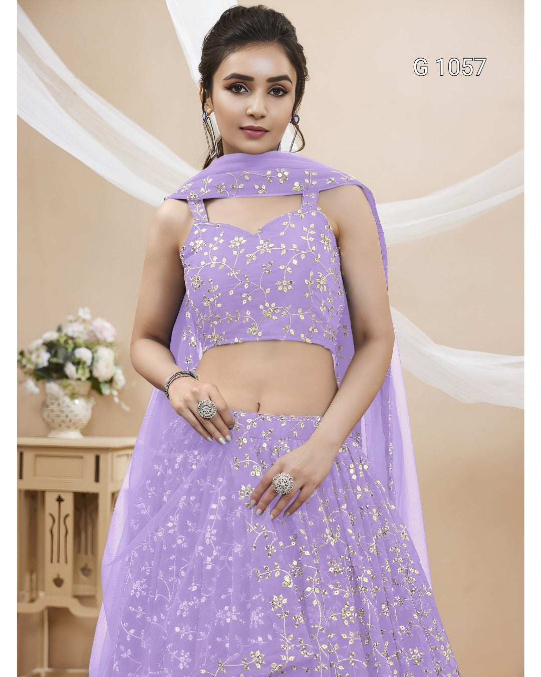 A woman models a lavender purple ethnic lehenga choli set with gold floral embroidery, featuring a sleeveless crop top, flared skirt, and matching dupatta.