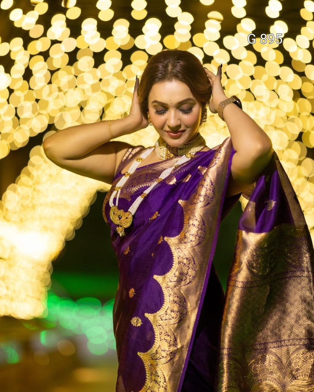 Woman in a purple and gold saree against a bokeh light background