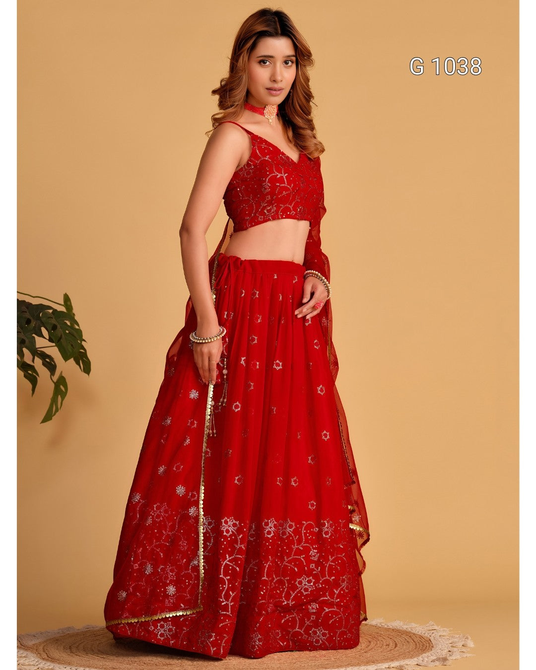 A woman modeling a red traditional Indian lehenga choli set with silver floral embroidery, standing against a solid beige background. The set includes a sleeveless crop blouse, a flared skirt, and a matching dupatta.