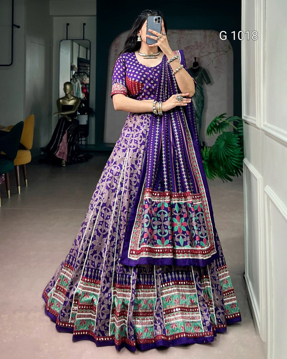 A woman takes a mirror selfie wearing a purple and silver embroidered Indian ethnic lehenga choli set with a heavily patterned flared skirt and matching dupatta. The set features purple, silver, red, and green embroidery.