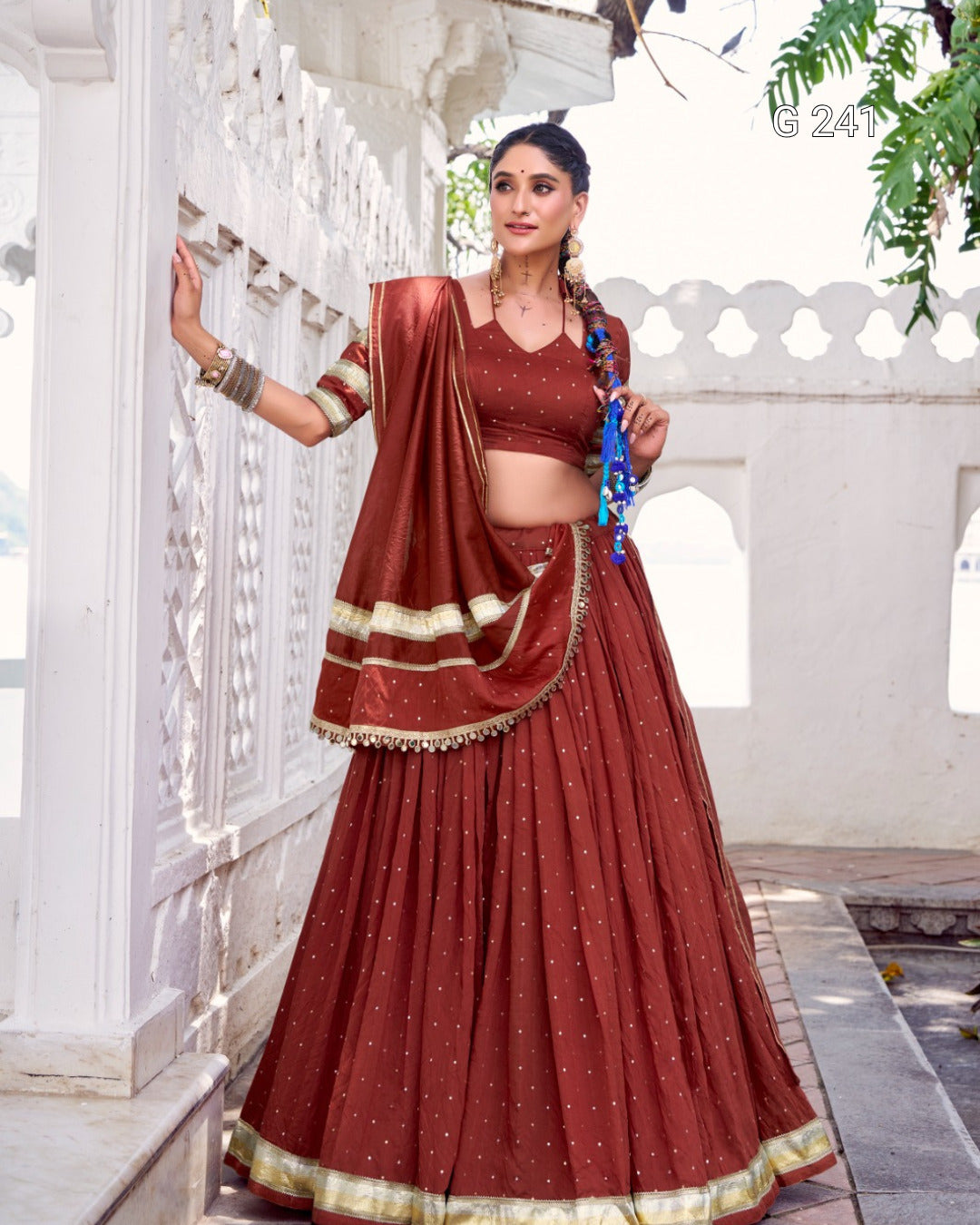 Woman in a traditional red and gold saree standing in an outdoor setting.