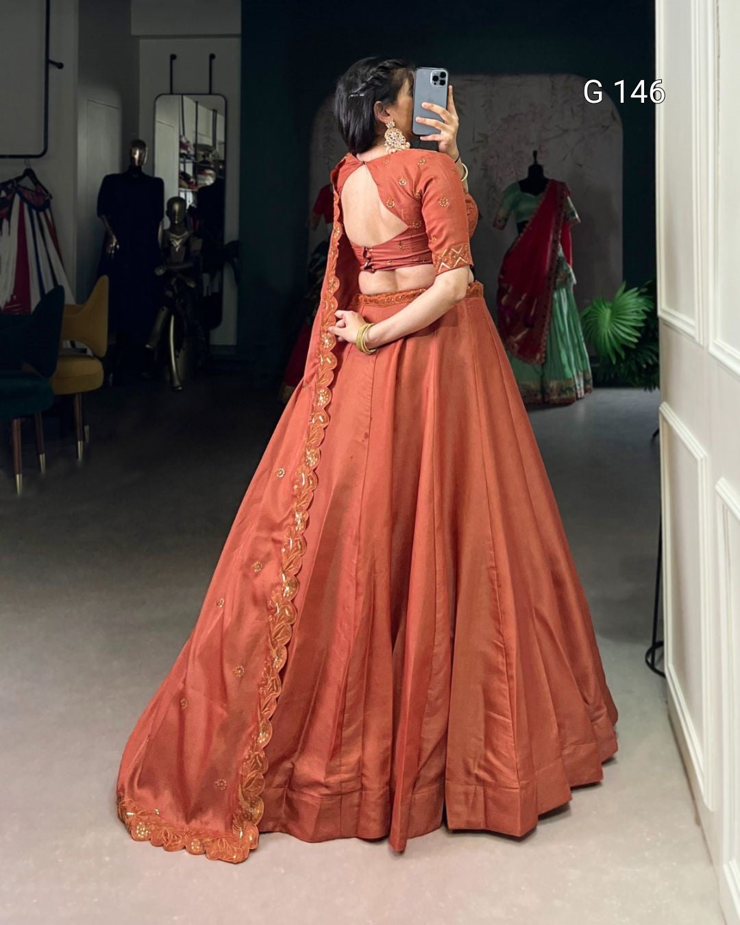 Person wearing a traditional orange saree with gold details, standing in a room.