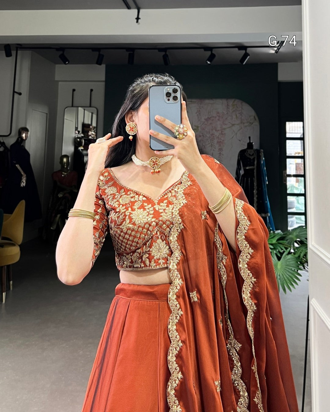 Person wearing an orange traditional outfit with gold embroidery in a room.