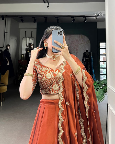 Person wearing an orange traditional outfit with gold embroidery in a room.