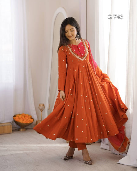 Woman wearing an orange traditional outfit with white patterns in a bright room.