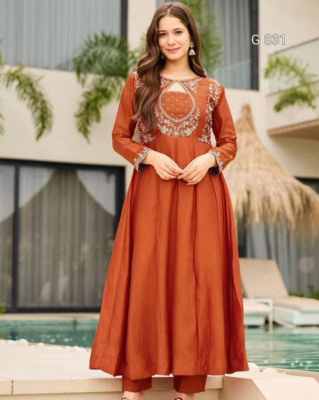 Woman wearing a rust-colored dress with intricate embroidery by a poolside.