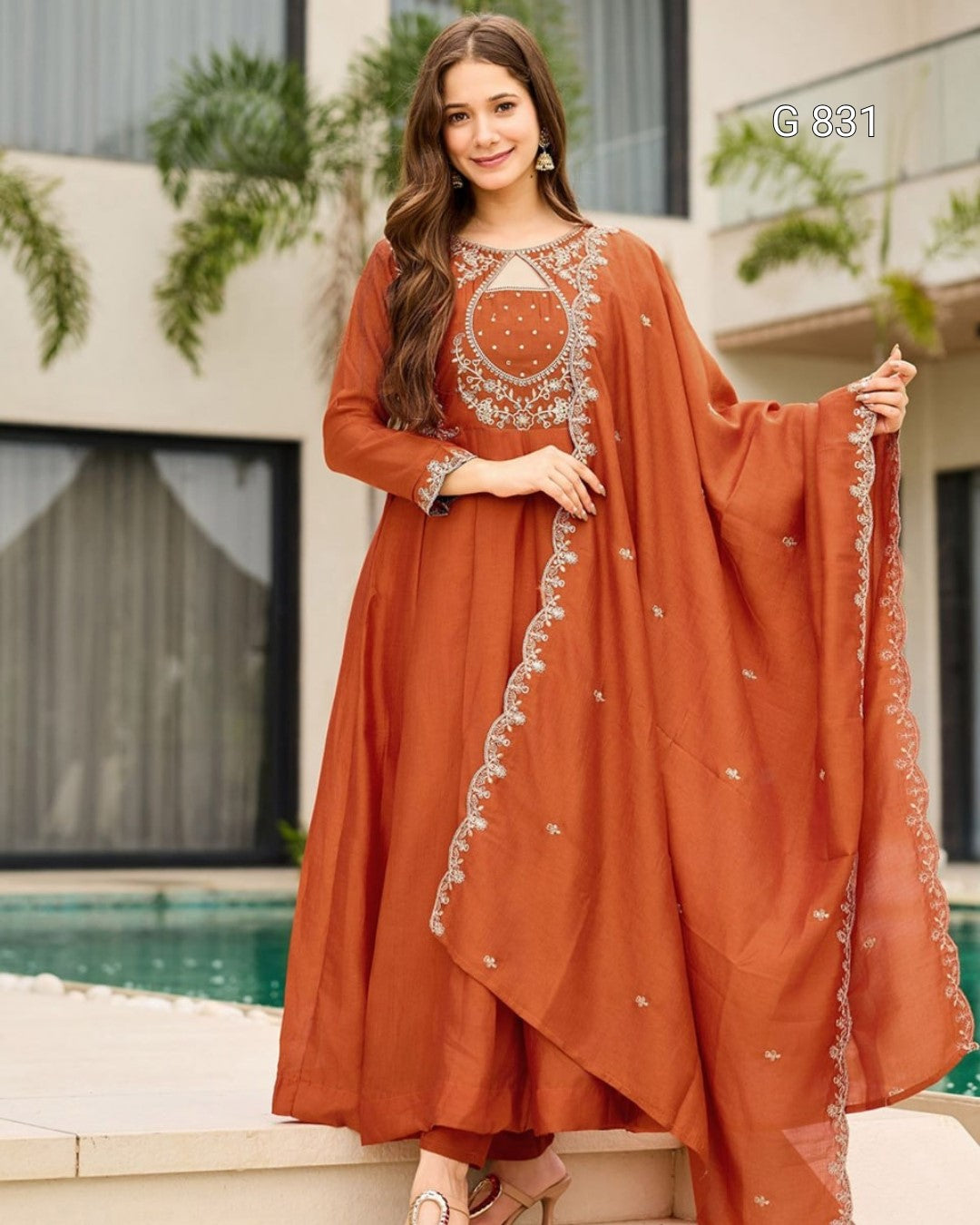Woman wearing a rust-colored traditional outfit with intricate embroidery by a poolside.