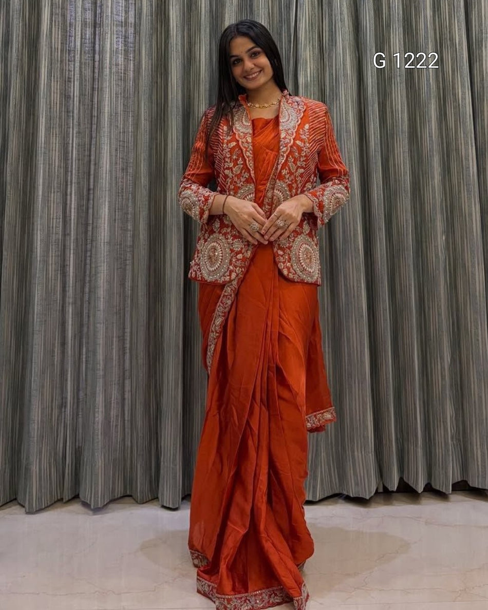 A woman modeling an orange traditional outfit with heavily embroidered beige and white details on the jacket and border, standing in front of gray pleated curtains. The text 'G 1222' is visible in the top right corner.