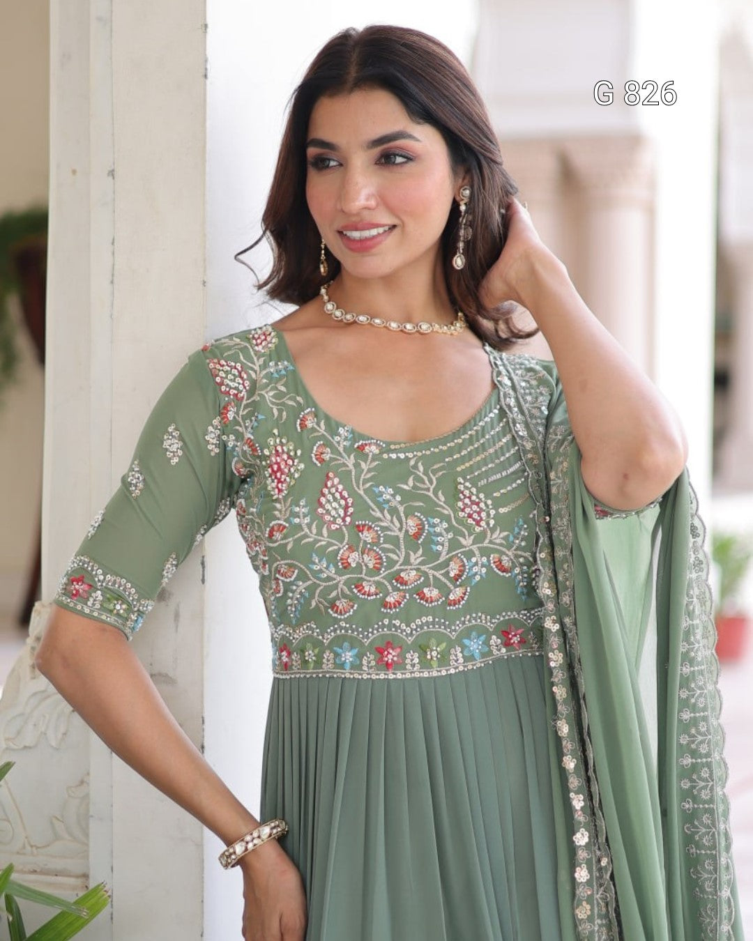 Woman wearing a green embroidered dress with a matching dupatta indoors.