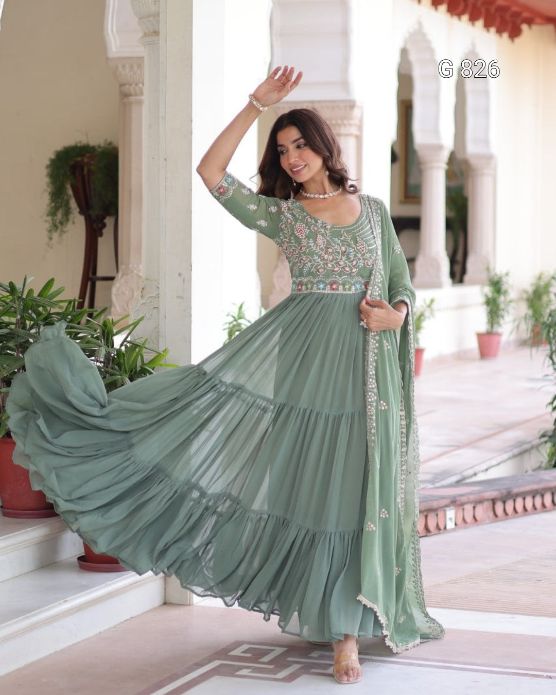 Woman in a green traditional outfit with floral patterns standing in an elegant indoor setting.