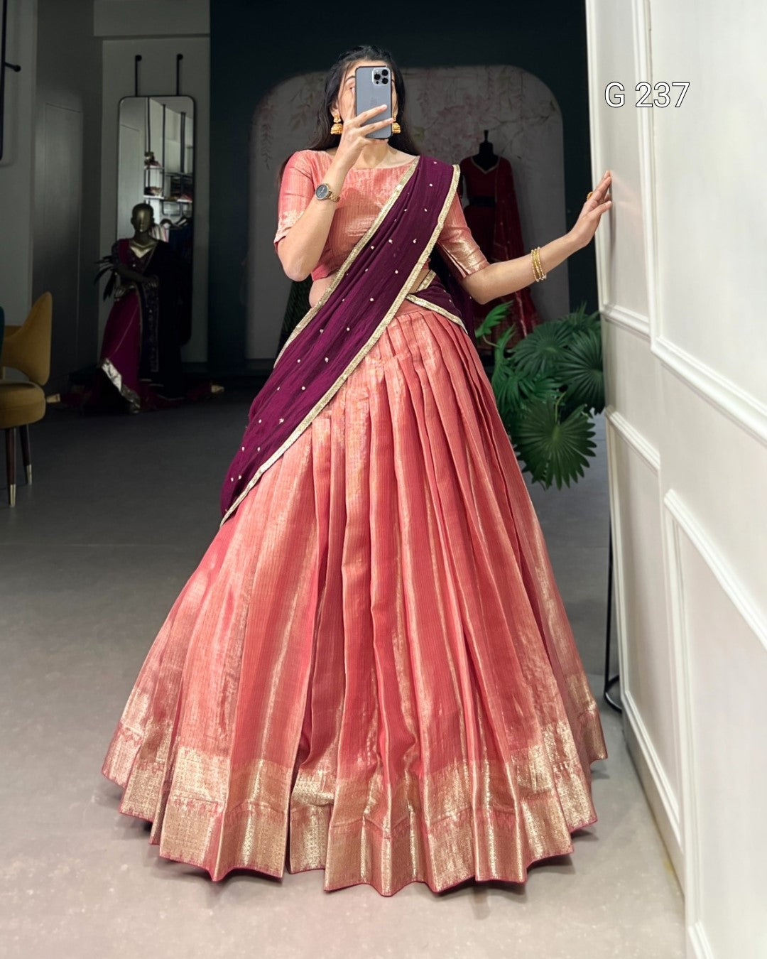Person wearing a pink saree with a purple blouse in a room.