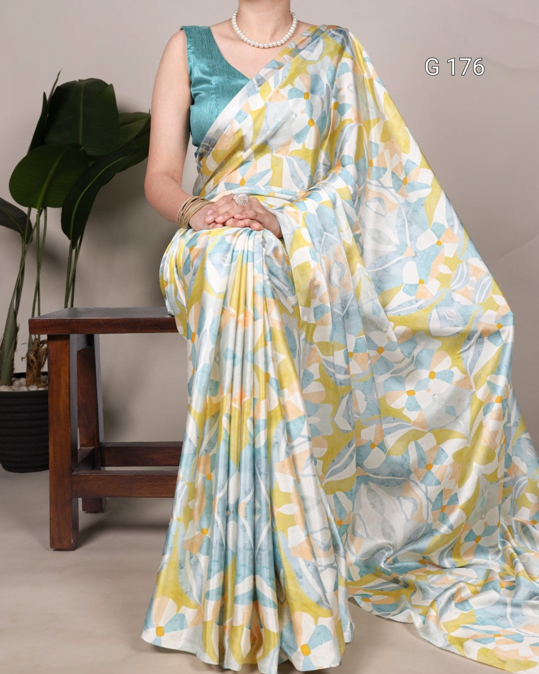 Woman wearing a floral saree with a green blouse, sitting on a wooden stool.