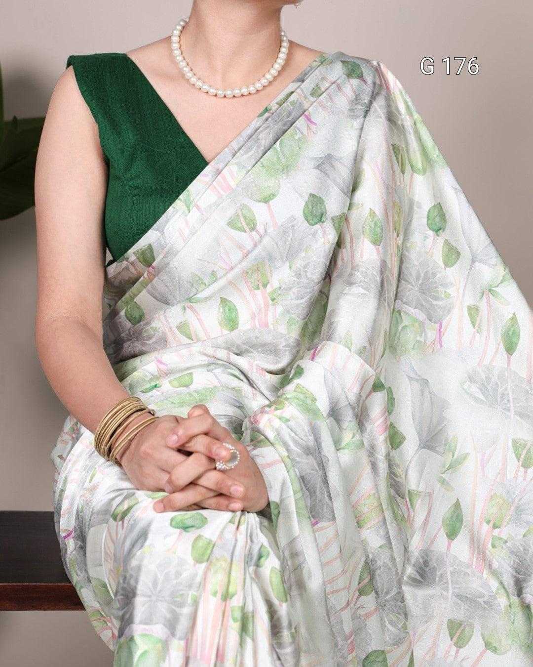 Woman wearing a green and white saree with a subtle pattern, pearl necklace, and gold bangles.