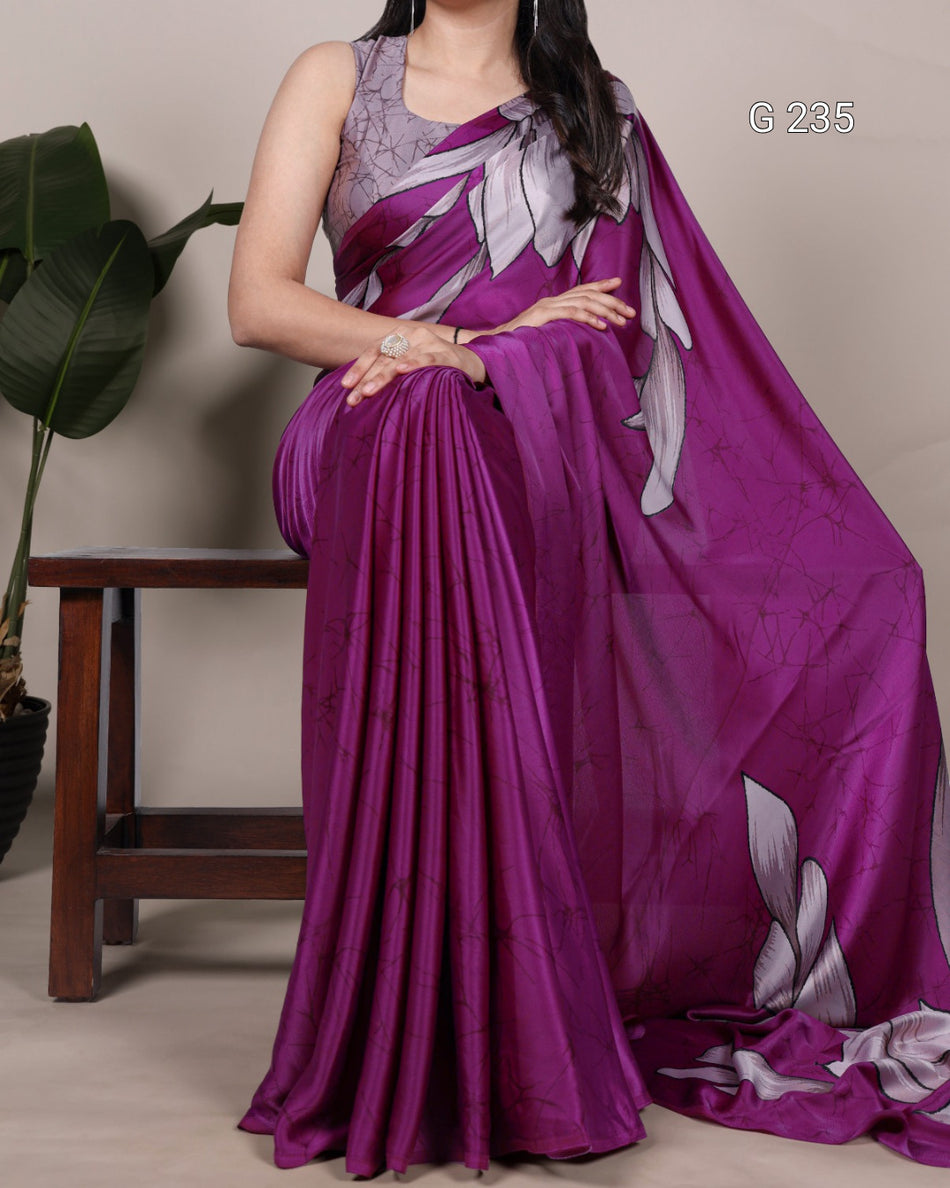 Woman wearing a purple saree with a floral blouse, sitting on a chair.