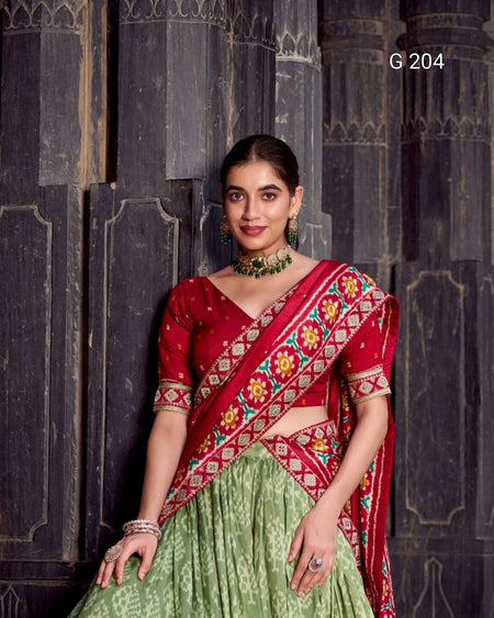 Woman wearing a red and green traditional outfit with intricate patterns against a dark stone wall.
