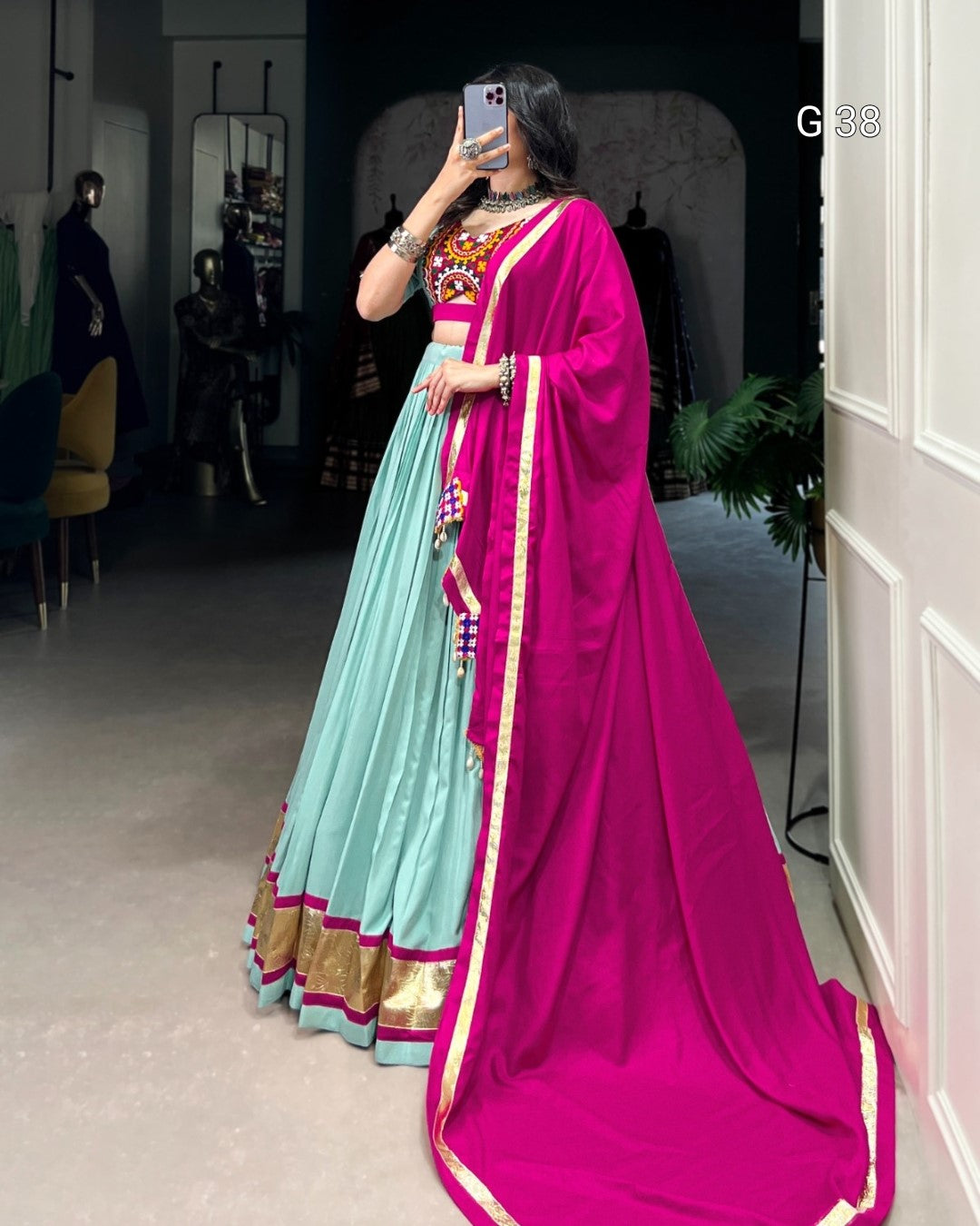 Person wearing a traditional outfit with a bright pink saree and light blue lehenga in an indoor setting.