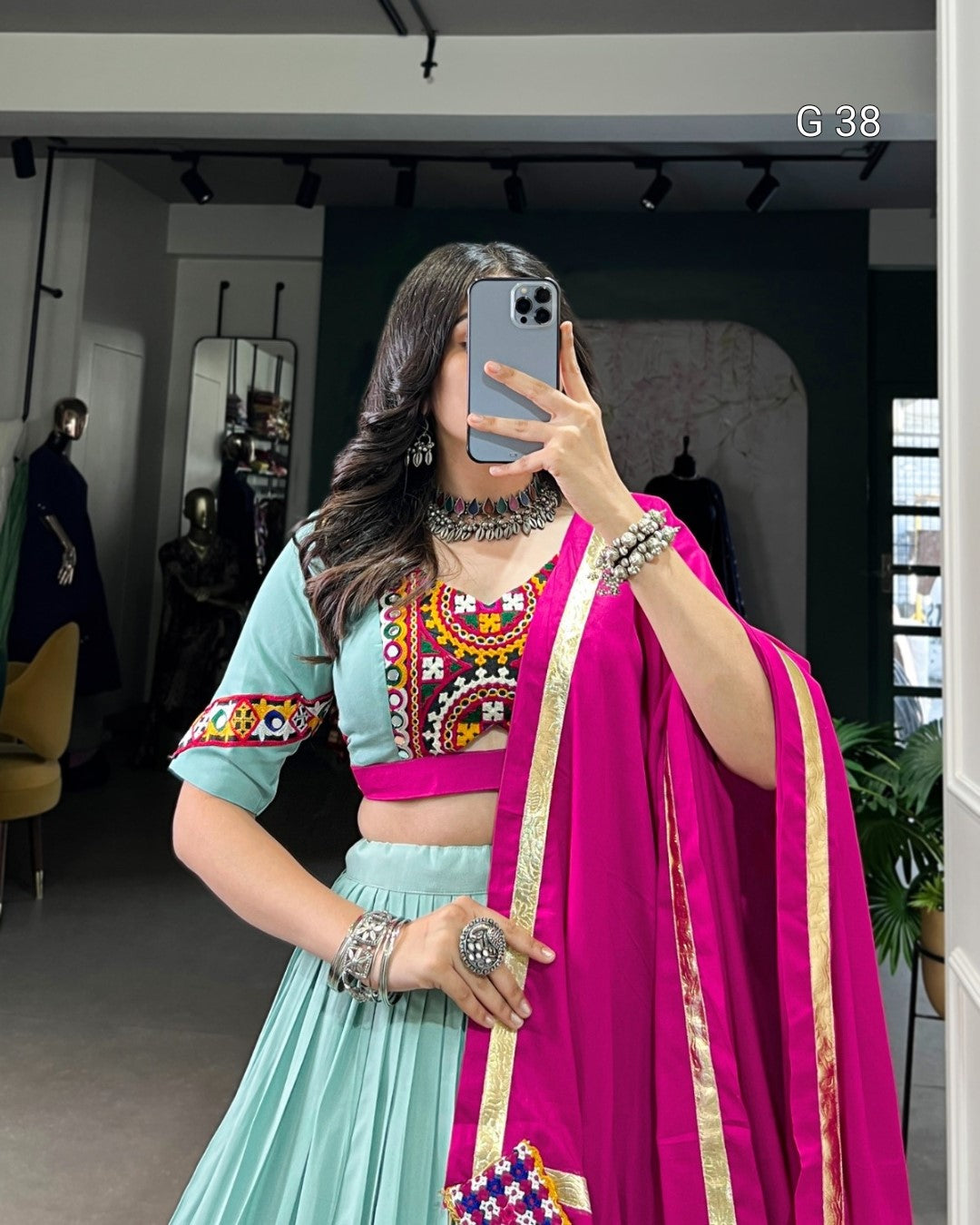 Person wearing a colorful traditional outfit with a pink dupatta in a mirror selfie.
