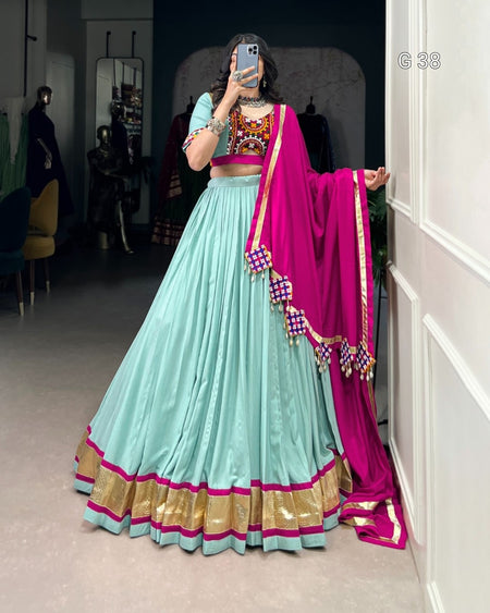 Person wearing a traditional outfit with a light blue lehenga and pink dupatta in a room.
