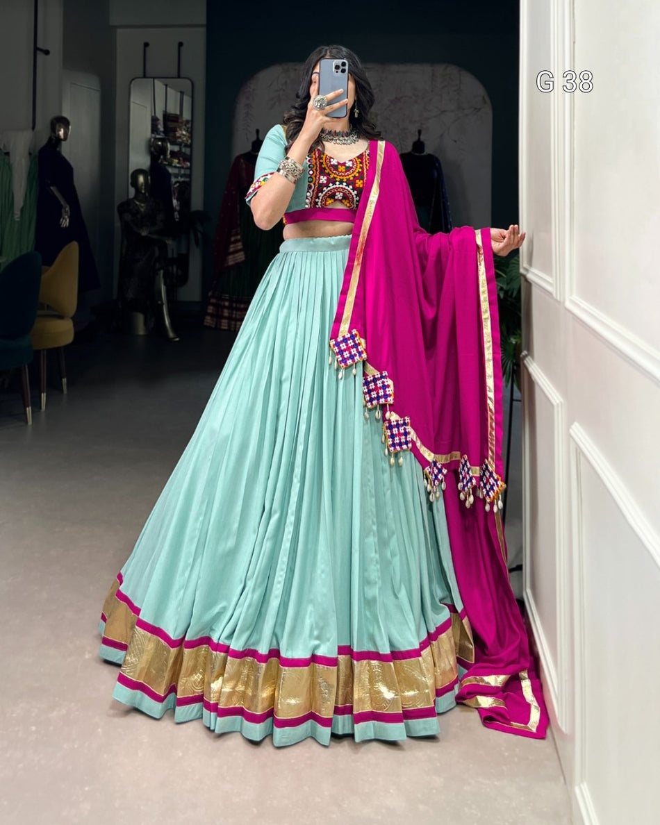 Person wearing a traditional outfit with a light blue lehenga and pink dupatta in a room.