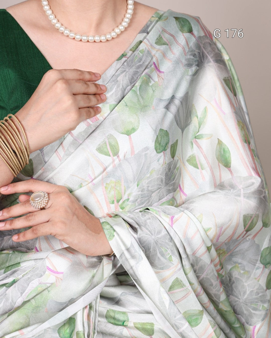 Woman wearing a green saree with floral patterns, pearl necklace, and gold bangles.
