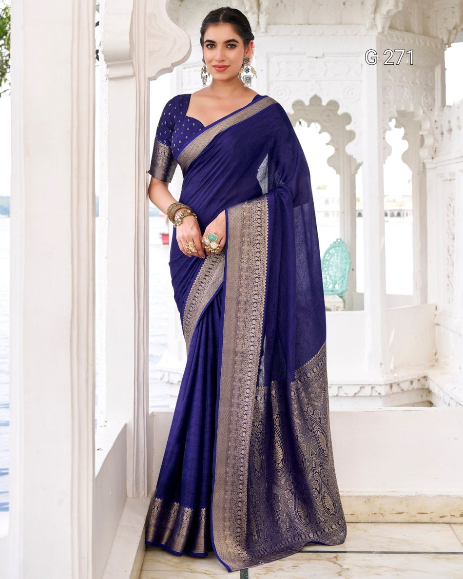 A woman models a royal blue silk saree with a wide metallic silver border and a matching blue embroidered blouse, standing in a white architectural corridor.