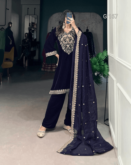 Person wearing a dark blue traditional outfit with intricate embroidery in a room.