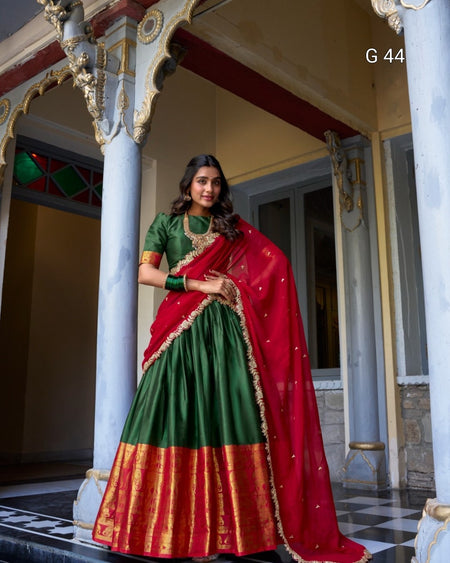 Woman in a green and red traditional outfit standing in an ornate indoor setting.