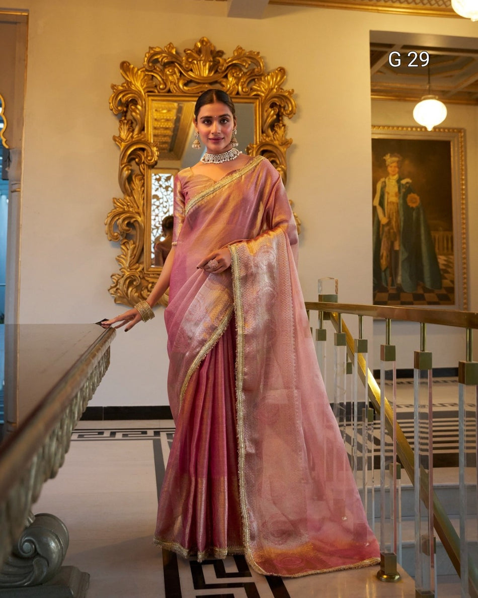 Woman in a pink saree standing in a decorated interior setting with a large mirror and artwork.