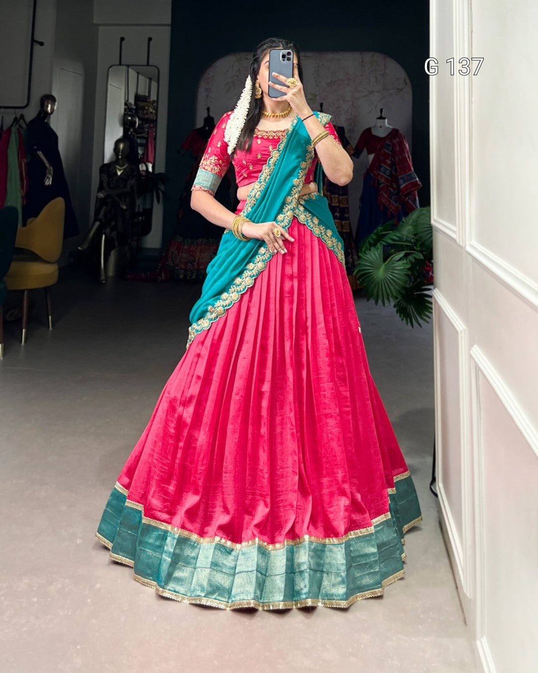 Person wearing a pink and blue traditional outfit in a room with clothing racks.