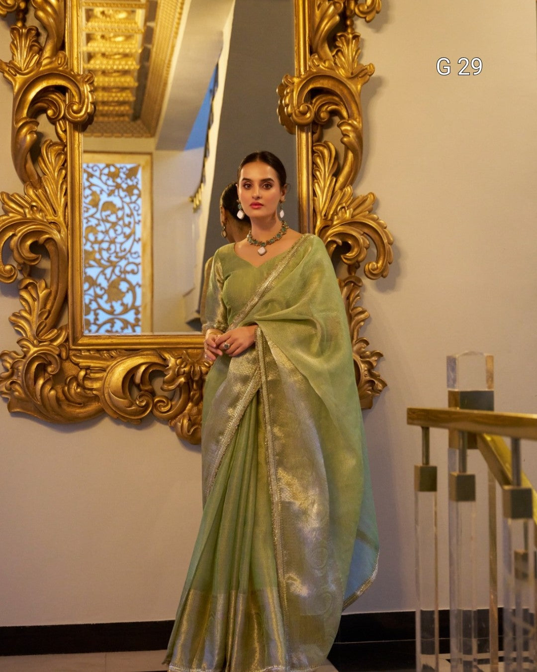 Woman in a light green saree standing in front of an ornate gold mirror.