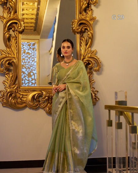 Woman in a light green saree standing in front of an ornate gold mirror.