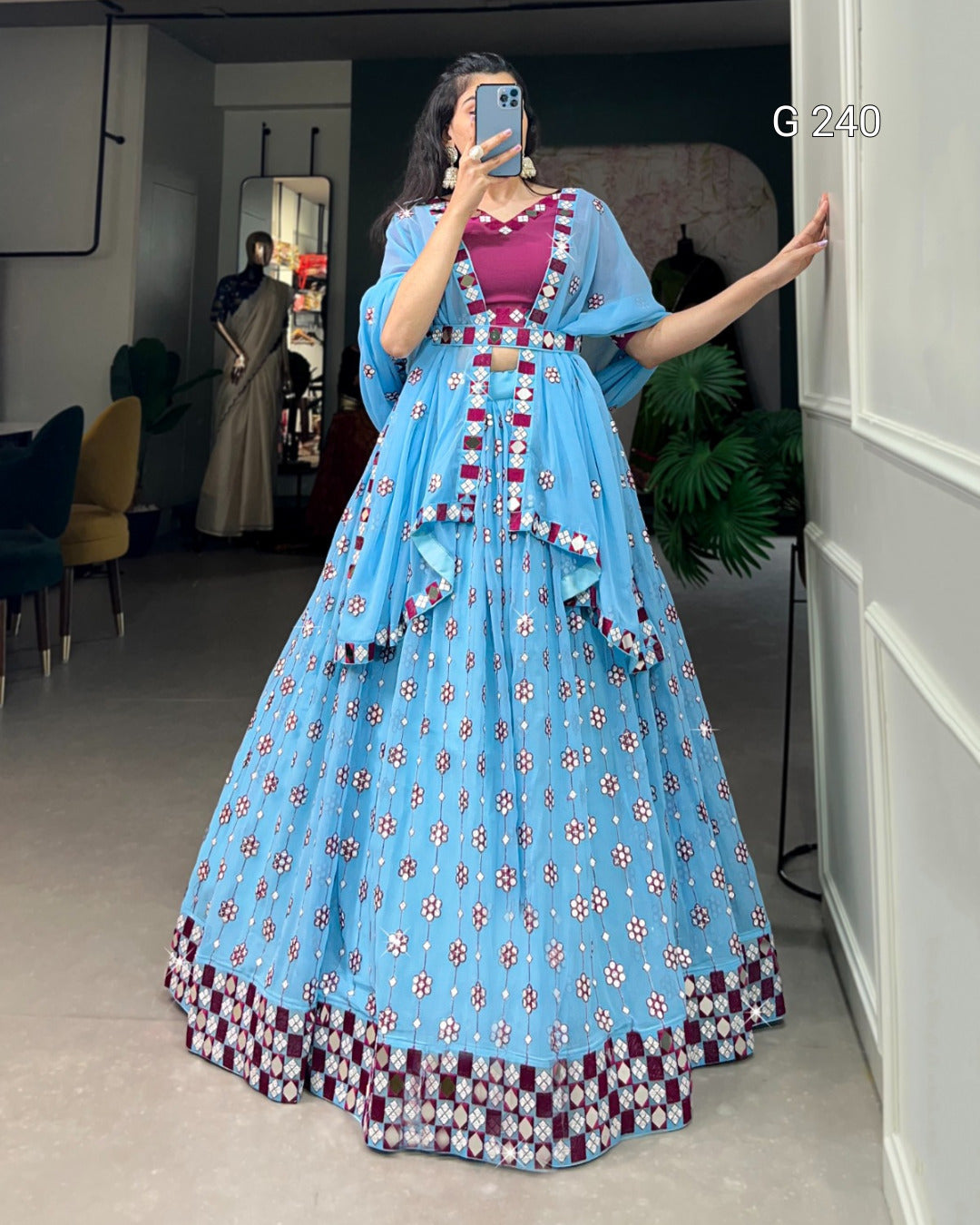 Woman in a blue floral dress taking a mirror selfie in a room.