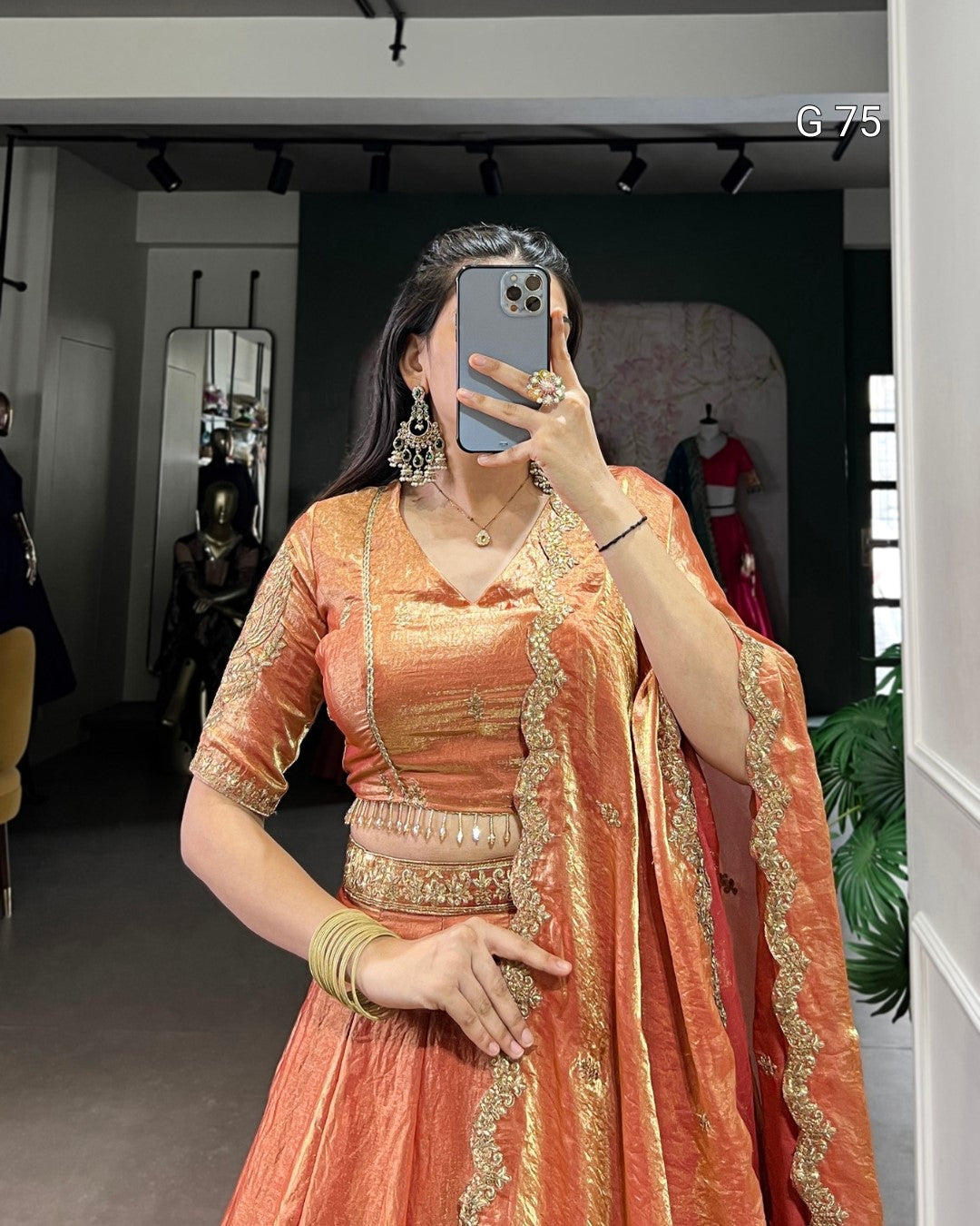 Woman taking a mirror selfie wearing an orange traditional outfit with gold embroidery.