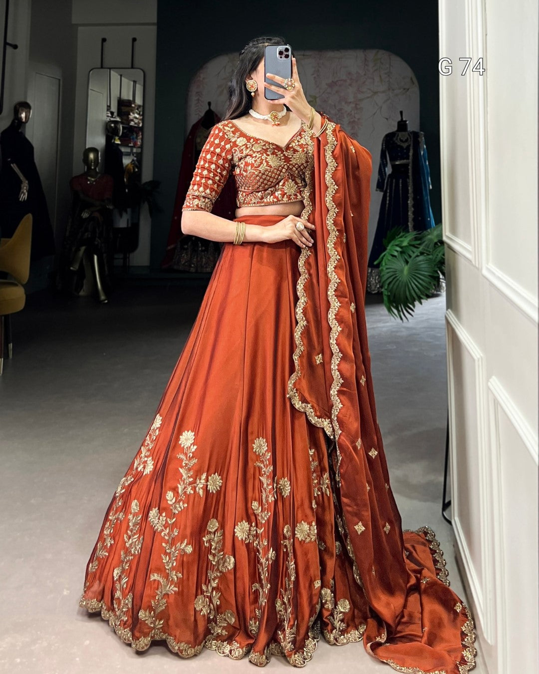 Woman in a traditional orange and gold embroidered outfit taking a mirror selfie.