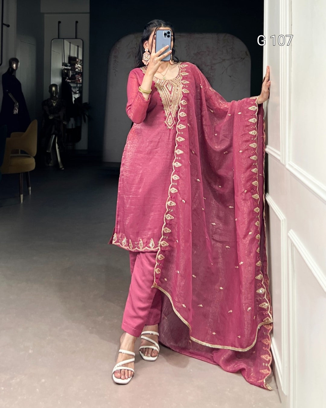 Person wearing a pink traditional outfit with gold embroidery in a room.