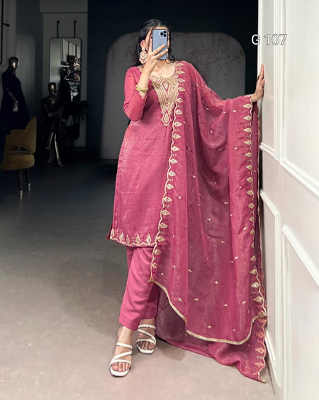 Person wearing a pink traditional outfit with gold embroidery in a room.