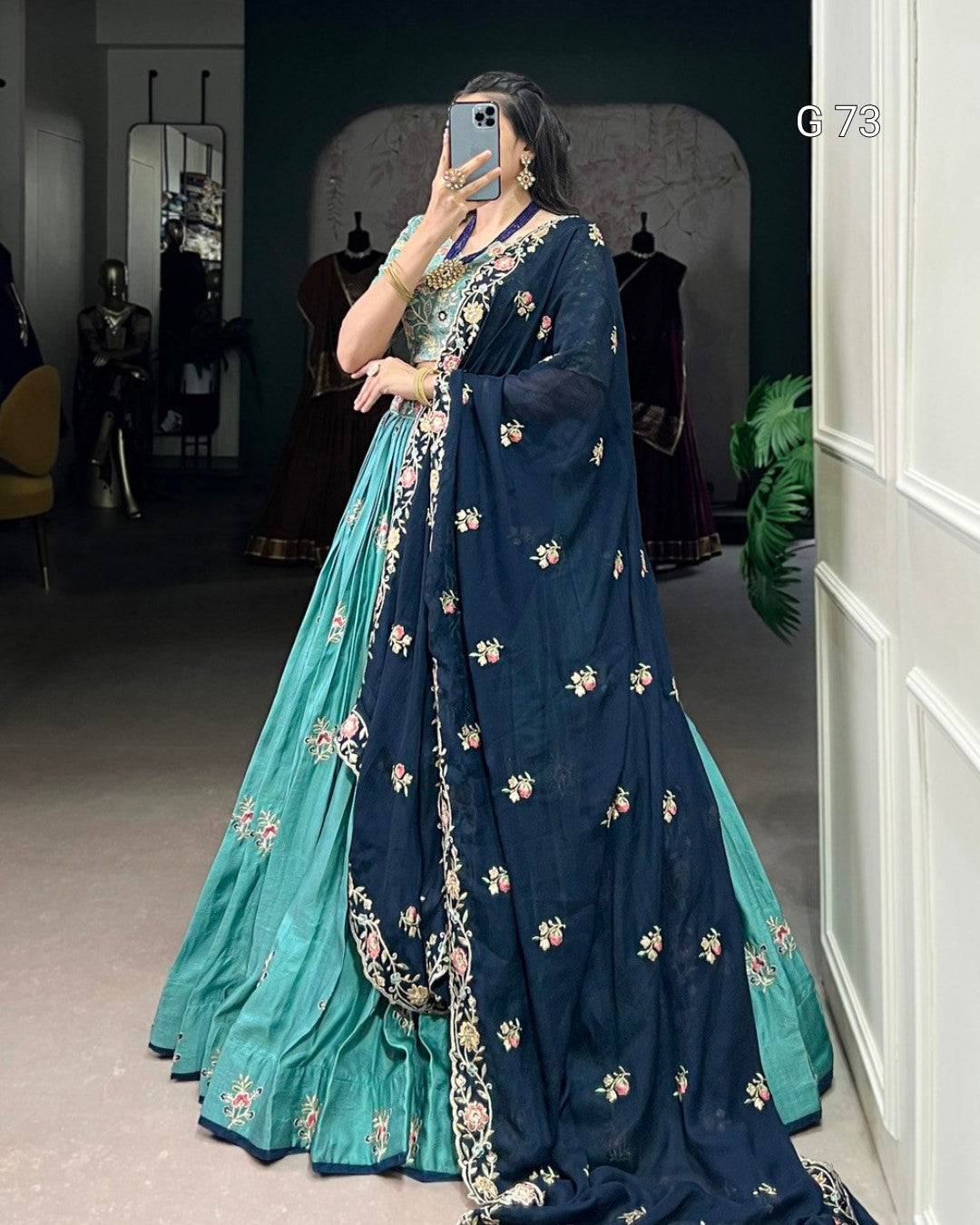 Woman wearing a blue and green saree with floral patterns in a room.