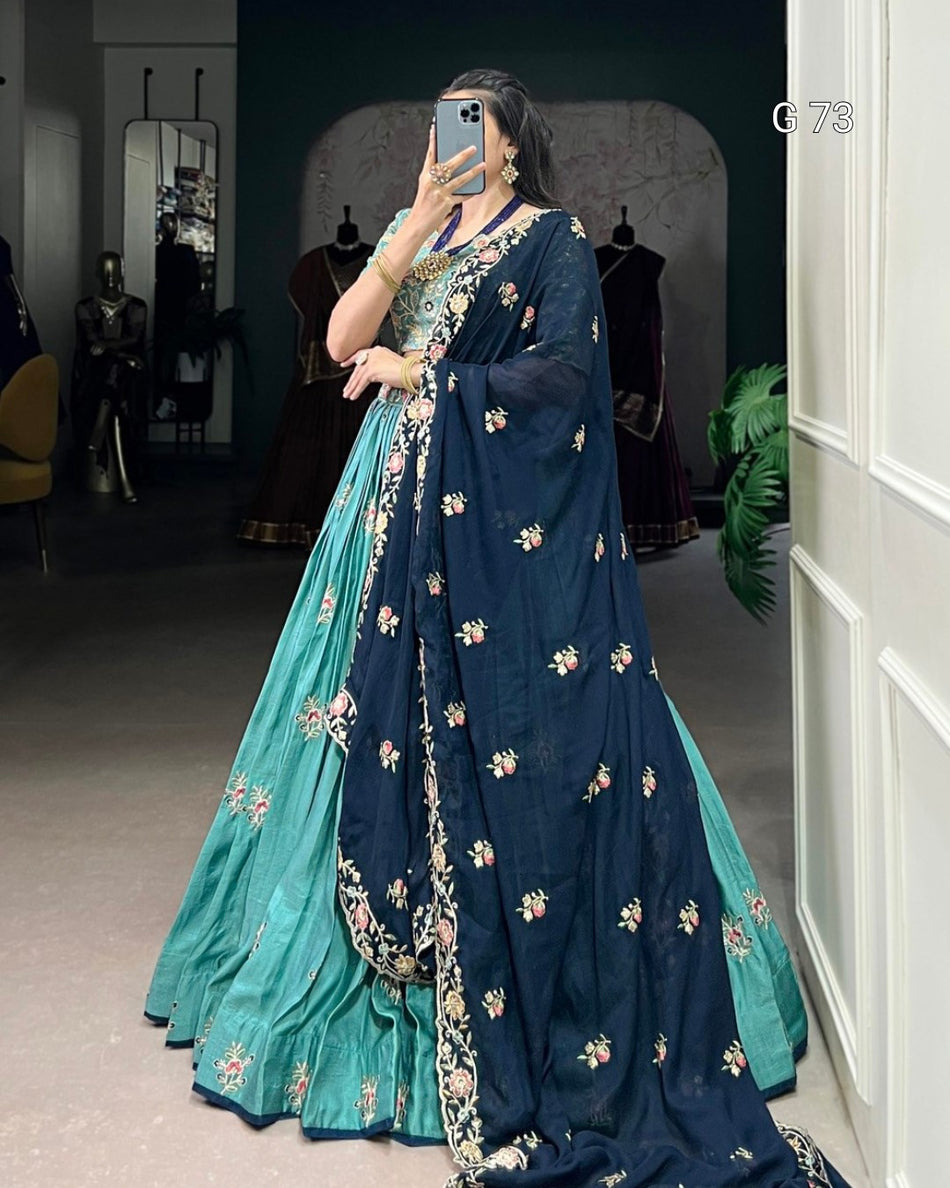 Woman wearing a blue and green saree with floral patterns in a room.