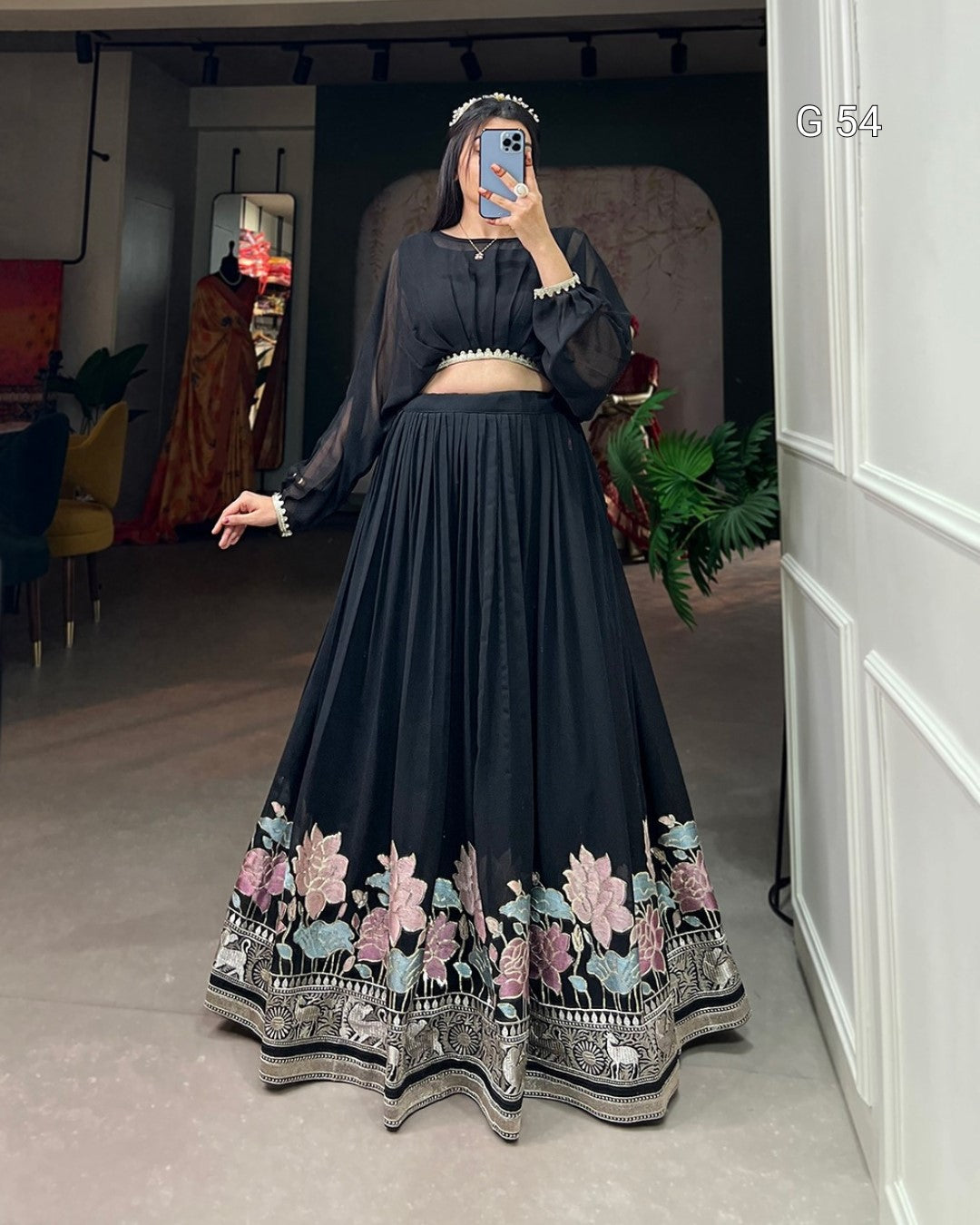 Person wearing a black embroidered outfit in a room with decor elements.
