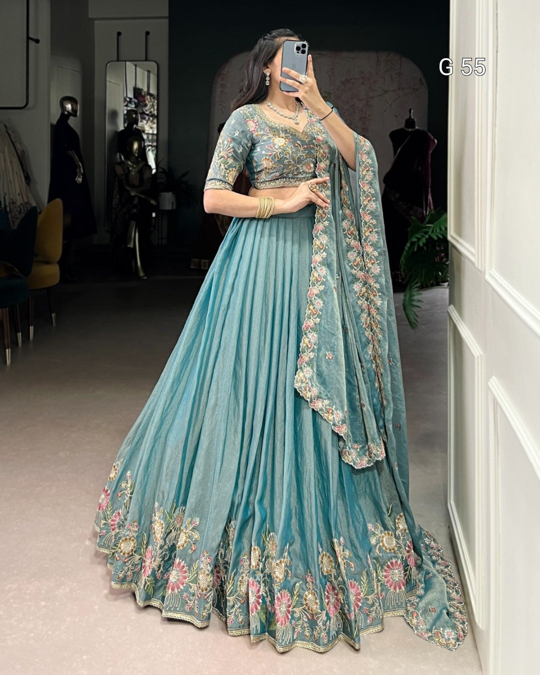 Woman wearing a light blue embroidered traditional outfit in a room.