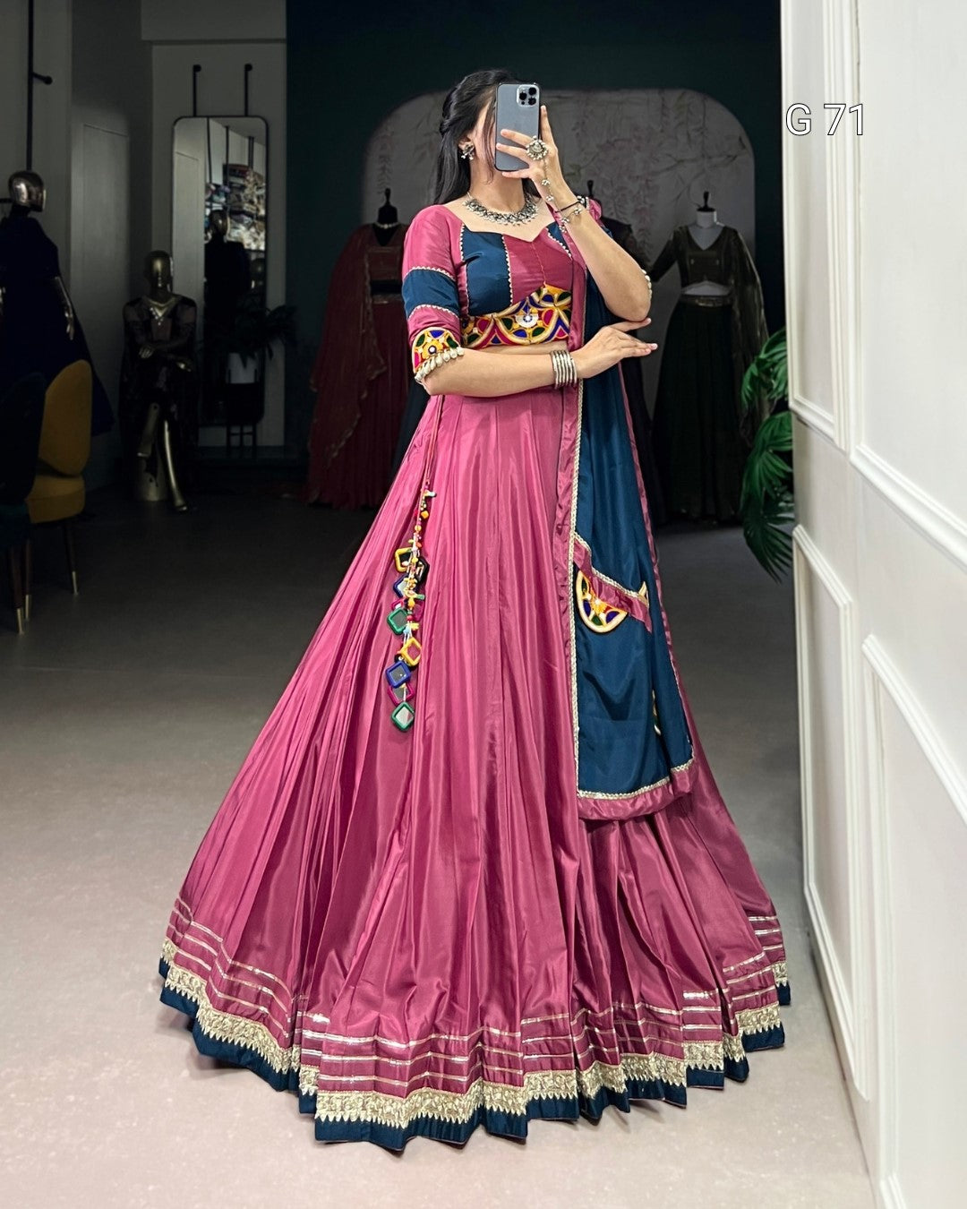 Person wearing a pink and blue traditional outfit with colorful patterns, standing in a room.