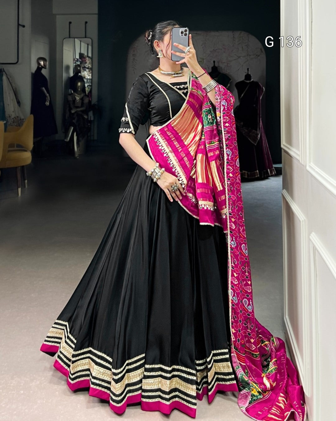 Woman wearing a black saree with pink and gold border, standing in a room.